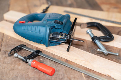 Electric jigsaw.and clamp paste on wooden table in workshop.