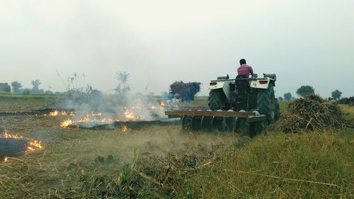 Tractor on grassy field with fire against sky