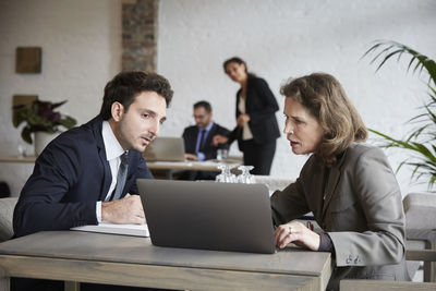 Senior female lawyer discussing over laptop with young businessman during meeting at office