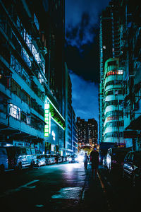 People walking on city street by buildings at night