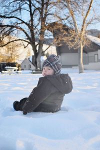 Cute baby boy sitting on snow covered field