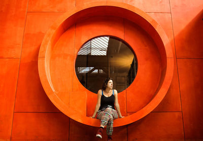 Full length of woman sitting on window of orange building