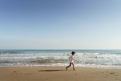 Rear view of woman standing at beach against clear sky