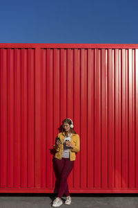 Full length portrait of smiling woman standing against red wall