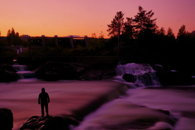 Silhouette man standing on rock against sky during sunset