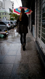 Full length rear view of woman walking on wet city