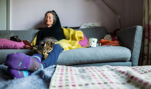 Woman using smart phone while relaxing with cat on sofa at home