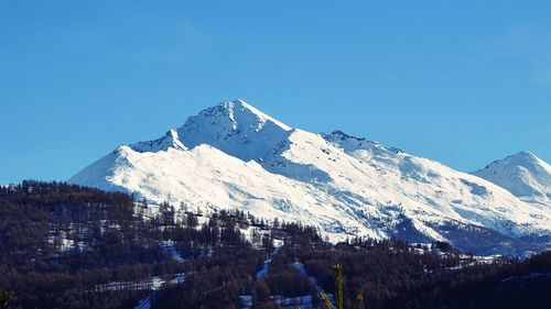 Low angle view of snowcapped mountains against clear blue sky