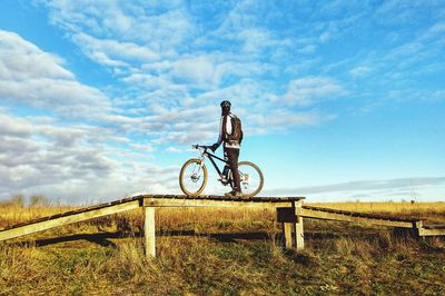 Man riding bicycle on field against sky