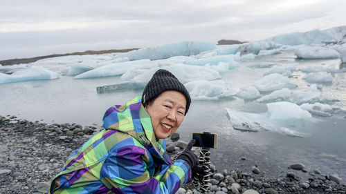 Portrait of smiling woman by glacier in sea during winter