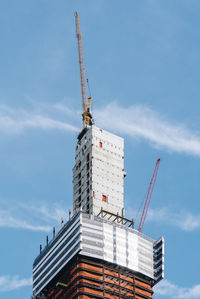 Low angle view of crane by building against sky