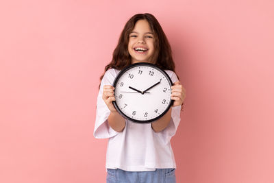 Portrait of woman holding alarm clock against coral background