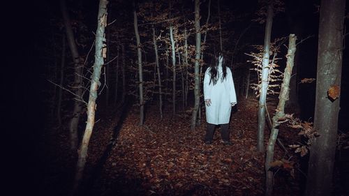 Woman standing by trees in forest at night