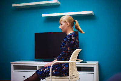 Side view of young woman sitting on chair at home