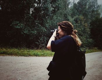 Young woman photographing through camera while standing on land