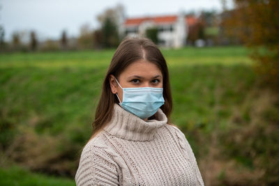 Portrait of young woman wearing mask standing on field