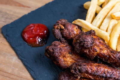 High angle view of fresh chicken wings and french fries with ketchup on table