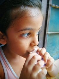 Close-up of girl eating chocolate against window
