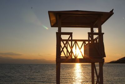 Silhouette built structure by sea against sky during sunset