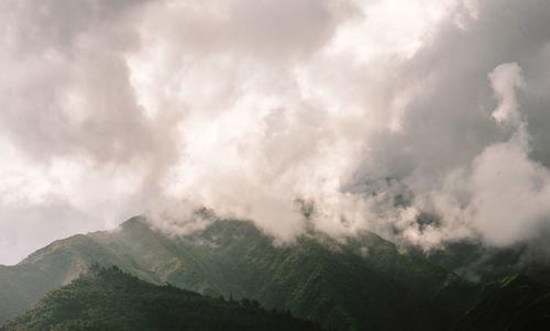 Scenic view of green mountains against cloudy sky