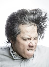 Close-up of frustrated man tossing hair against white background