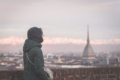 Rear view of woman standing against cityscape during sunset