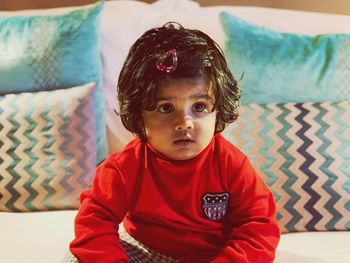 Cute baby girl looking away while sitting on bed at home