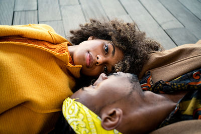 Top view of trendy african american man and woman in bright coat lying opposite with face to face looking at each other