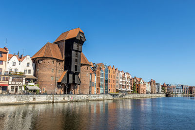 Buildings by river against clear blue sky