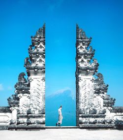 Man standing by historical structure against blue sky