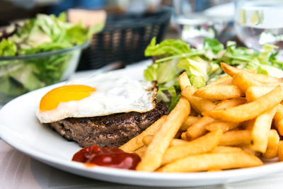 Close-up of fried egg with french fries and meat served on table