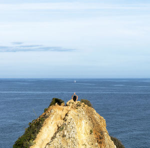 Rear view of woman doing yoga on rock formation against sea