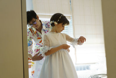 Mother helping daughter getting dressed for communion at home