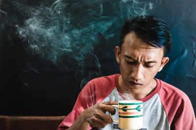 Close-up of man having drink while sitting against wall