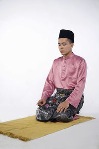 Young man looking away while sitting against white background