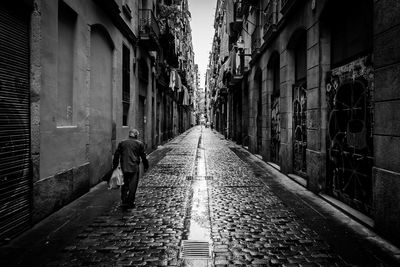 Rear view of man walking on narrow street amidst buildings