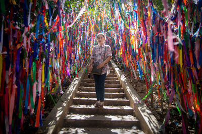 Full length portrait of woman standing amidst colorful prayer ribbons on steps