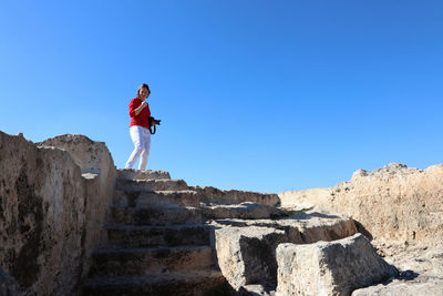 Low angle view of woman standing on rock against sky