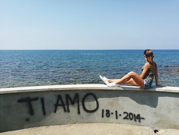 Woman sitting by sea against clear sky