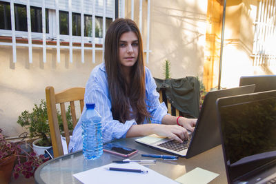 Young woman using phone while sitting on table