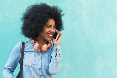 Smiling young woman using phone while standing against blue wall