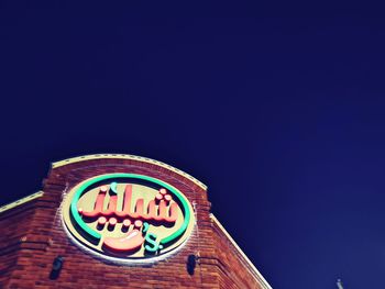 Low angle view of illuminated sign against clear blue sky