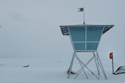 Snow covered land by sea against clear sky