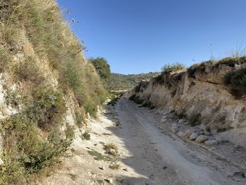 Road passing through landscape against clear blue sky