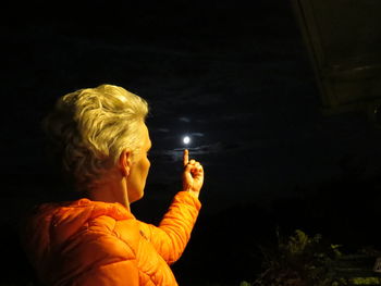 Optical illusion of woman holding moon at night