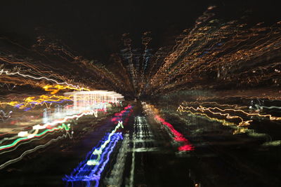 Light trails by trees against sky at night