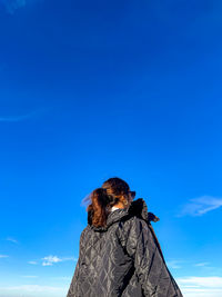 Low angle view of woman sitting on cliff against sky