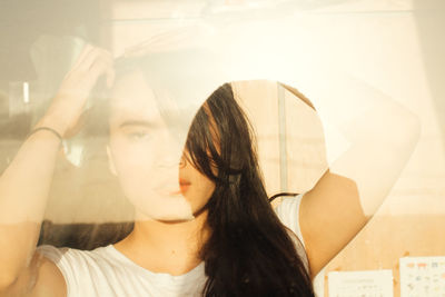 Close-up portrait of young woman at home seen through glass window