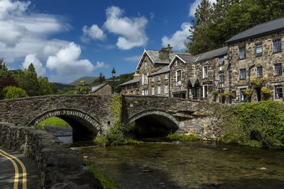 Arch bridge over river amidst buildings against sky