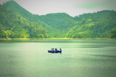 People in boat sailing on river against mountains